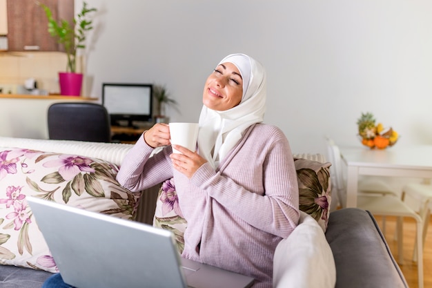 Arab Young business woman sitting at her desk at home, working on a laptop computer and drinking coffee or tea