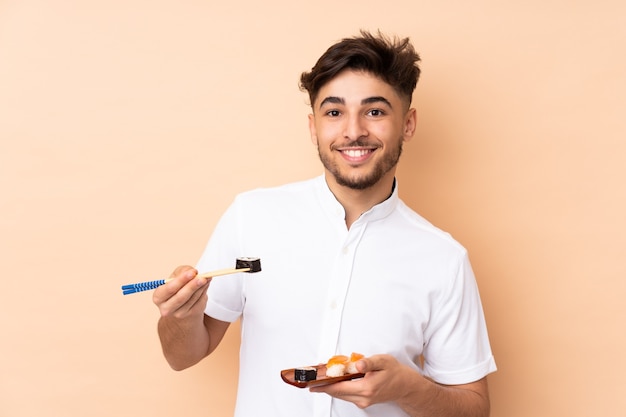 Arabian man eating sushi isolated on beige wall