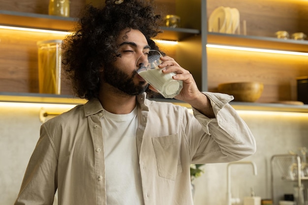 Arabian man enjoys drinking milk in glass in kitchen at home