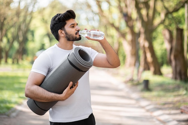 Arabian man in sport clothes drinking water from bottle