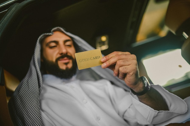 An arabian man in a traditional clothing in a car holding a credit card