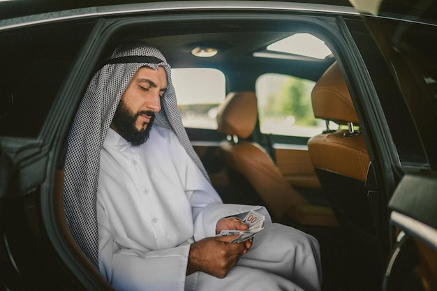 An arabian man in a traditional clothing in a car holding money