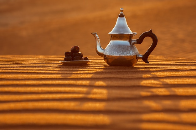 Photo arabian teapot and dates in the desert at a beautiful sunset 