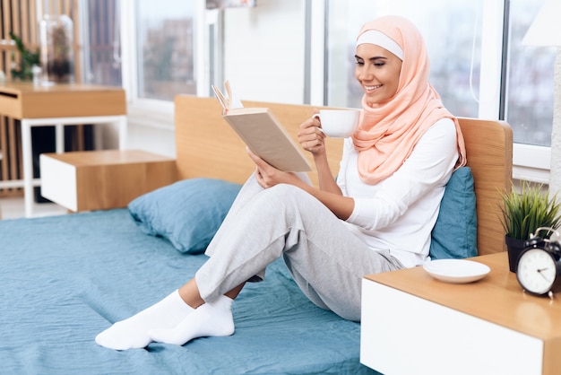 Arabian woman is drinking tea and reading a book.