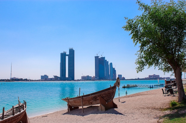 Arabic dhow boat on the sandy shore in front of skyscrapers