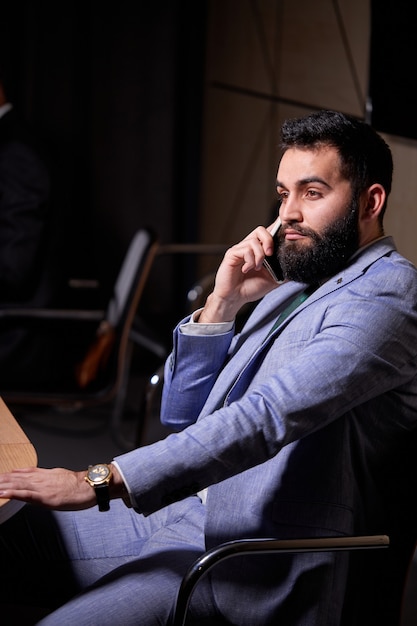 Arabic male sits listening to colleagues speech , looking at side, wearing elegant formal suit, discussing startups and finance, at interracial business meeting