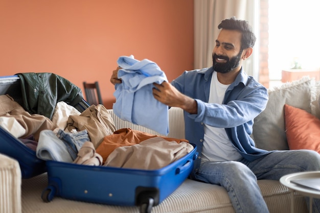 Arabic man packing clothes in suitcase preparing luggage at home