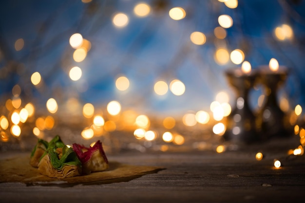 Arabic sweets on a wooden surface Candle holders night light and night blue sky with crescent moon in the background