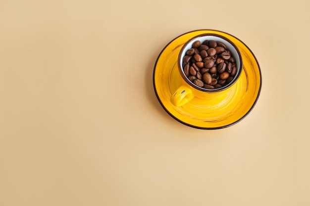 Arabica coffee beans in a bright designer yellow cup with saucer pastel beige paper