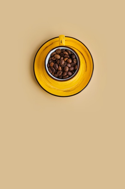 Arabica coffee beans in a bright designer yellow cup with saucer pastel beige paper