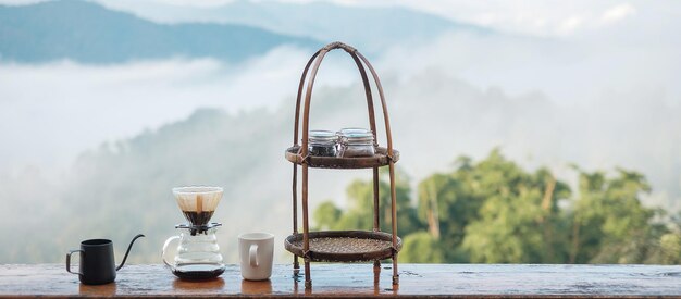 Arabica coffee brewing by Vintage coffee drip equipment set on wooden table in the morning with mountain and nature background