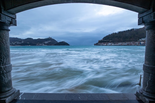 An arch with sculptures with crazy sea waves at a port in San Sebastian, Spain