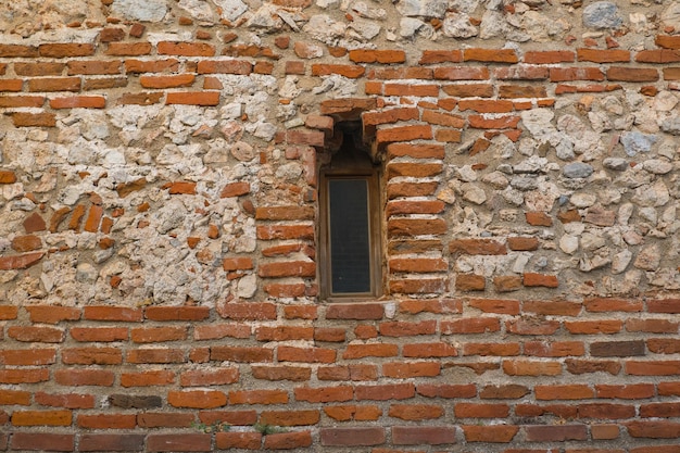 An arched window in a fortress or castle made of red stone Architecture of old stone buildings