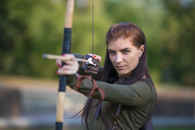 Archery woman with bow shooting on the forest