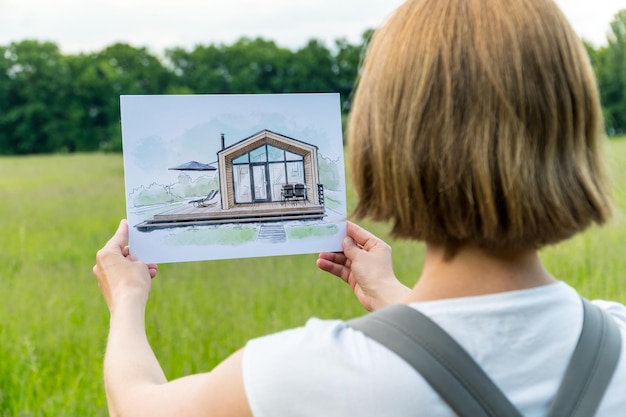 Architect holding barn house hand drawn sketch in front of a plot of land