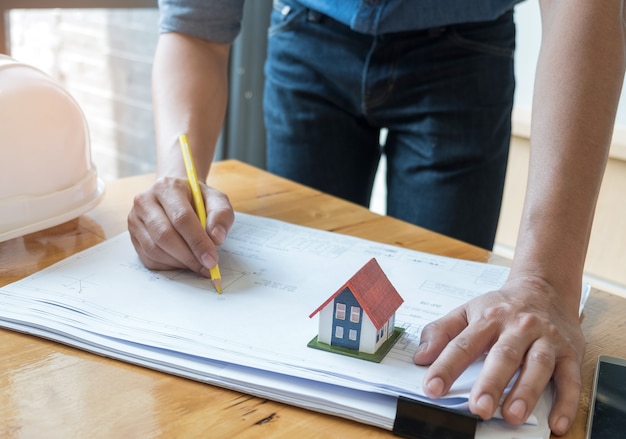 Architect holding a yellow pencil drawing house plan with model house on the floor plan.