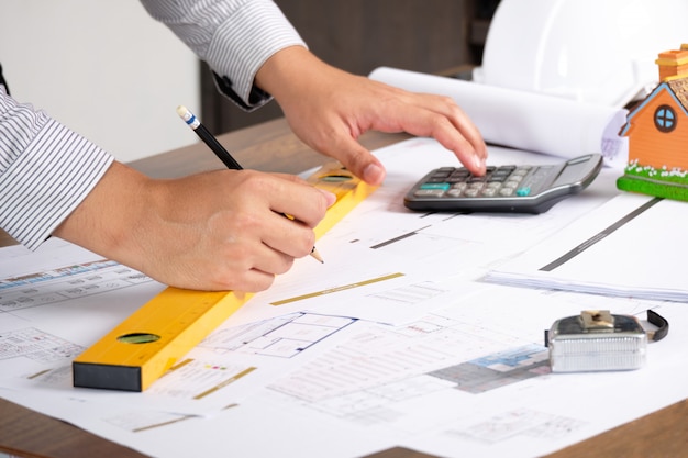 Architect is drawing construction plans on Blueprint paper with pencil and using Calculator.