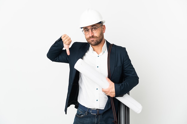 Architect man with helmet and holding blueprints isolated on white background showing thumb down with negative expression