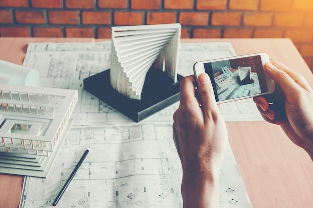 Photo architect using smart phone photograph model building in office.