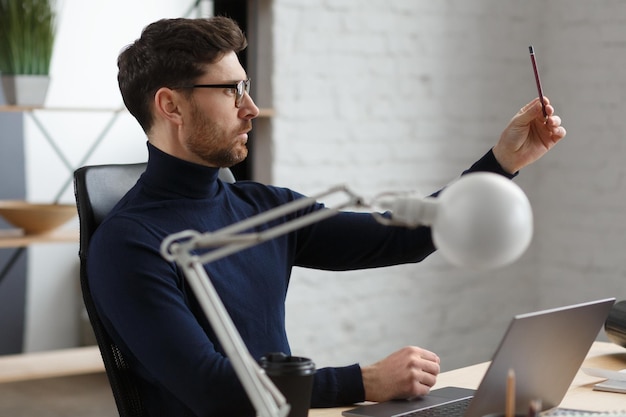 Architect working in office with laptop.Engineer thinks over architectural plan, searching new ideas for construction project. Portrait of handsome bearded man sitting at workplace. Business concept.