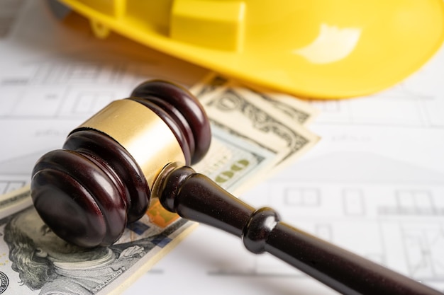 Architectural house plan project blueprint and Judge gavel hammer with yellow helmet and US dollar banknotes Engineer and construction law and justice