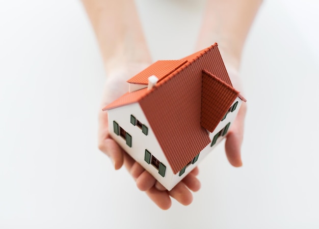 architecture, building, construction, real estate and property concept - close up of hands holding house or home model