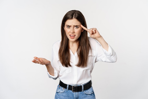 Are you dumb. Annoyed woman scolding, roll finger over head and staring at camera, bothered by someone crazy, standing over white background