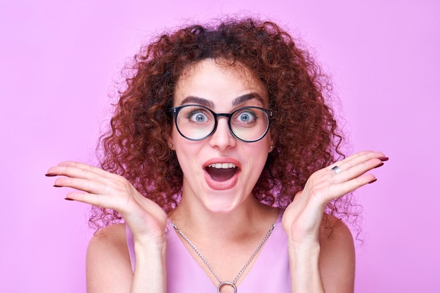 Photo armenian shocked positive girl raises palms from joy with glasses and open mouth heard amazing news happy to receive incredible surprise present isolated in pink studio