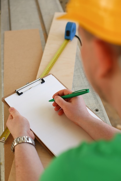 Arms of worker making notes on clipboard with green pen