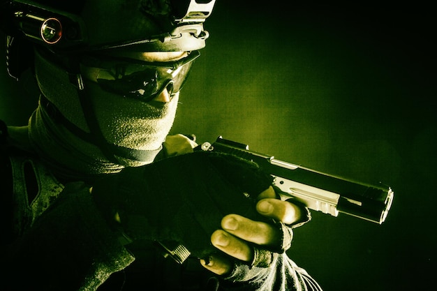 Army counterterrorism squad police SWAT team fighter hiding identity behind mask and glasses wearing helmet with night visiondevice creeping in darkness aiming service pistol during mission