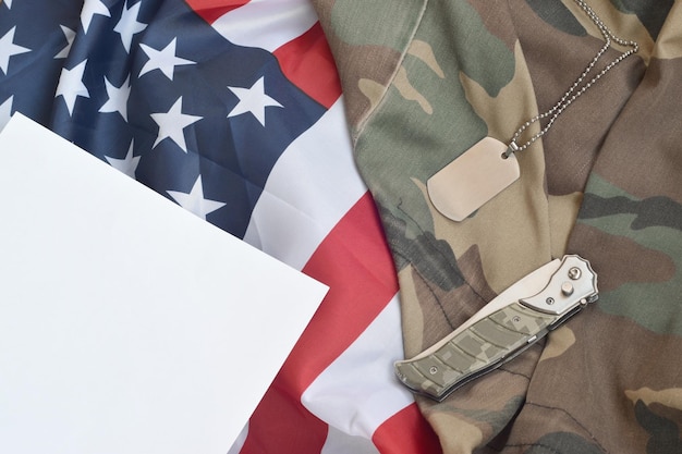 Army dog tag token and knife lies on Old Camouflage uniform and folded United States Flag