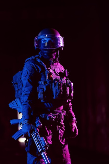 Army soldier in Combat Uniforms with an assault rifle and combat helmet night mission dark background Blue and purple gel light effect