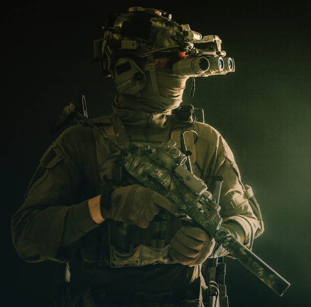 Army special forces tactical group fighter moving in darkness using radio headset looking through four lens nightvision thermal imaging device on helmet armed small submachine gun with silencer