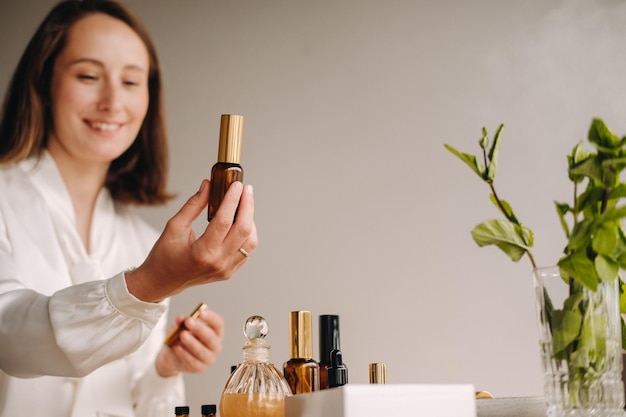 The aromatherapist girl is sitting in her office and holding a bottle of aromatic oils there are essential oils on the table