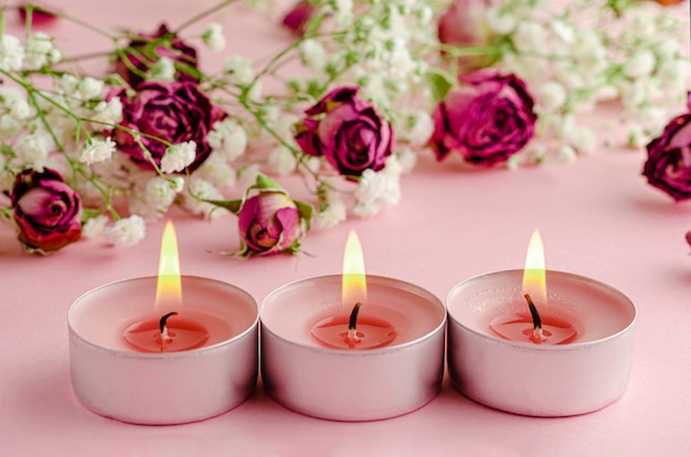 Aromatherapy concept. Three burning candles and dry roses on pink.