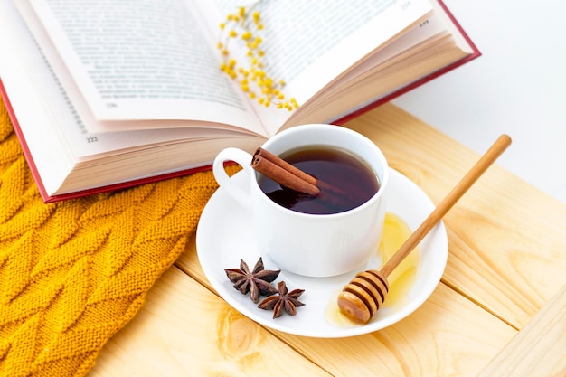 Aromatic hot cinnamon tea covered with a warm scarf on a wooden autumn background honey dipper with honey comfortable reading a book