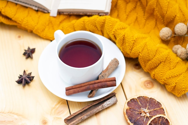 Aromatic hot cinnamon tea covered with a warm scarf on a wooden autumn background.