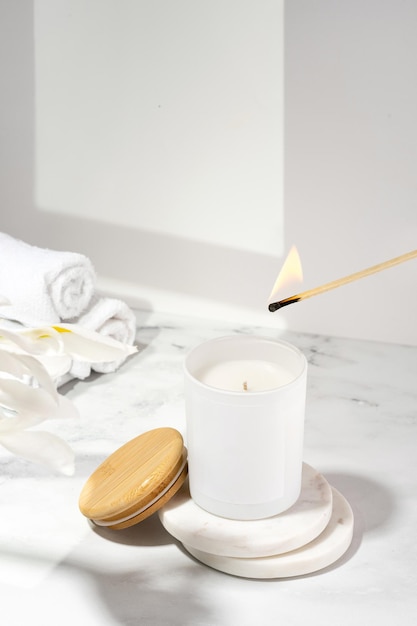 An aromatic soy wax candle is set on fire with match An ecological and vegan candle bath accessories and a wooden cap on a marble table Aromatherapy scent relax Still life composition concept