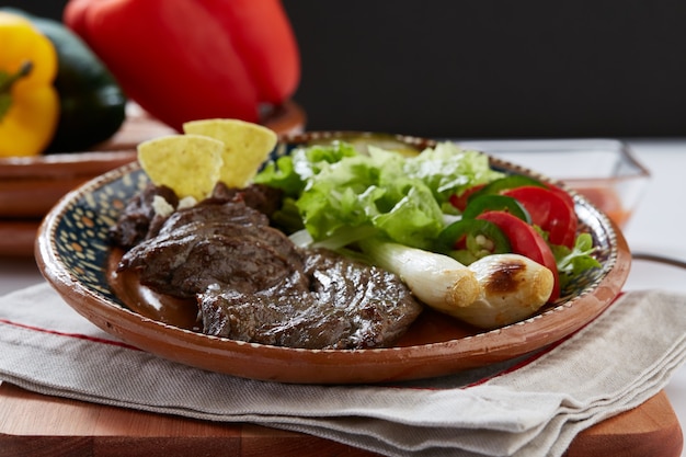 Arrachera con frijoles refritos cebollinas y ensalada servido en plato de barro