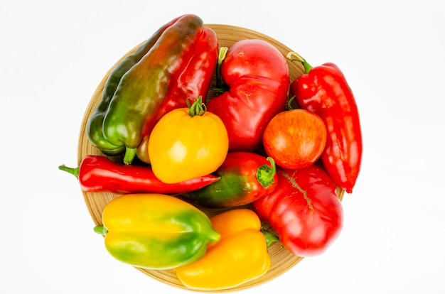 Arrangement of colorful fresh assorted bell peppers and tomatoes in wooden plate on white background. Studio Photo.