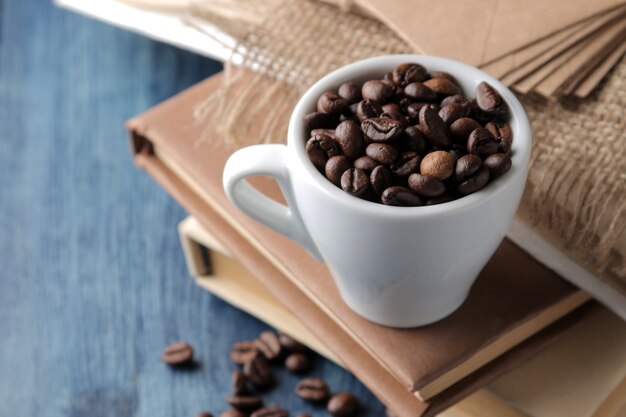 Arrangement with coffee beans in a cup and books on a blue wooden table.