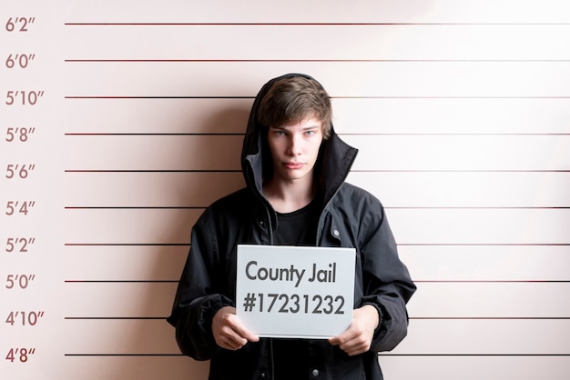 The arrested prisoner young man holding a placecard in front of the height chart