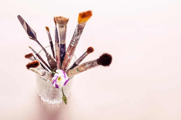 Art brushes and flowers in glass on table. Selective focus.