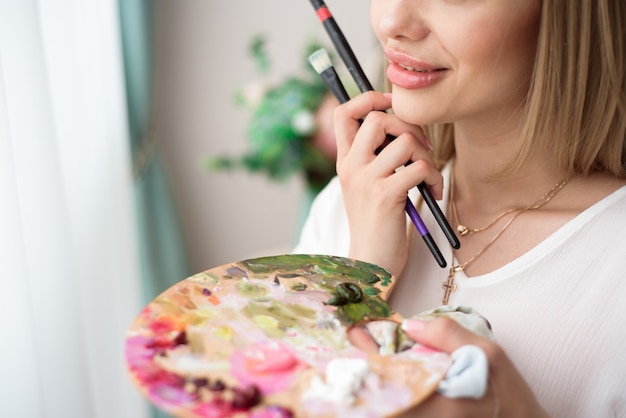 Photo art, creativity, hobby, job and creative occupation concept. female artist posing in front of window and painting with oil or acrylic paint