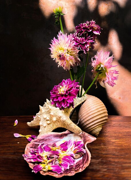 The art of flower arrangement Romantic bouquet with xAdahlias dahlia petals in a sea shell and a starfish on a wooden table on an old rusty background in the rays of sunlight