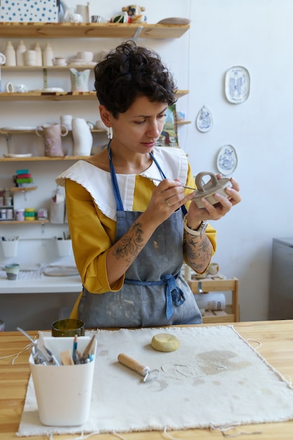 Art hobby and business young woman wear apron concentrated on molding ceramic jar in pottery studio