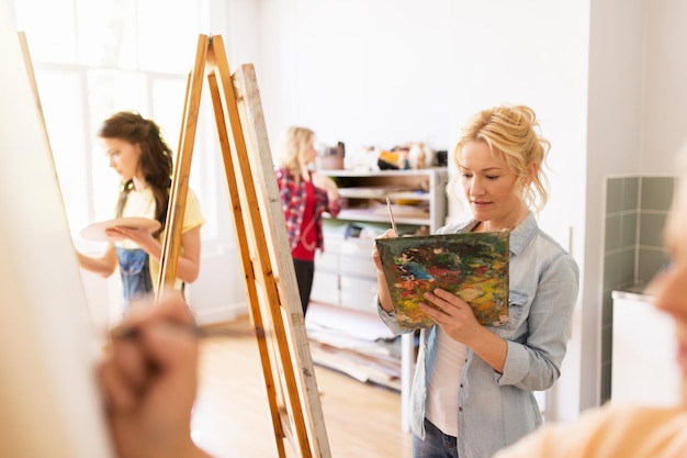 Photo art school, creativity and people concept - woman artist with easel, paint brush and palette painting at studio