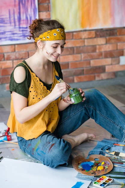 Photo art therapy and leisure. creative young female painter sitting on floor, washing paintbrush