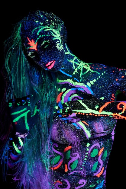 Art woman body art on the body dancing in ultraviolet light. Bright abstract drawings on the girl body neon color. Fashion and art woman, out of focus