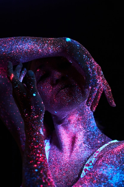 Art woman cosmos in ultraviolet light. Entire body is covered with colored droplets. Girl posing in the dark. Noise, out of focus